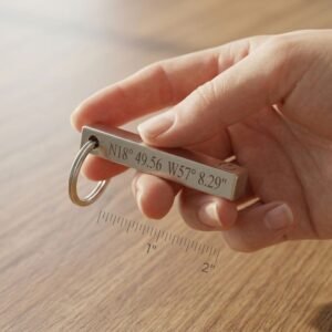 Close-up of hand holding custom engraved bar keychain with coordinates text and compact size reference