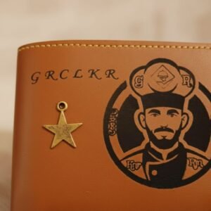 Detailed close-up of engraved chef design and metallic star charm on brown leather wallet — can be customized with your photo.