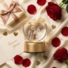 Personalized apple-shaped 3D crystal lamp with couple photo engraved, glowing warm yellow light, romantic gift setup with roses and gift box.