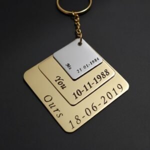 Engraved metal couple keychain with stacked square plates and gold finish, photographed on a teal background
