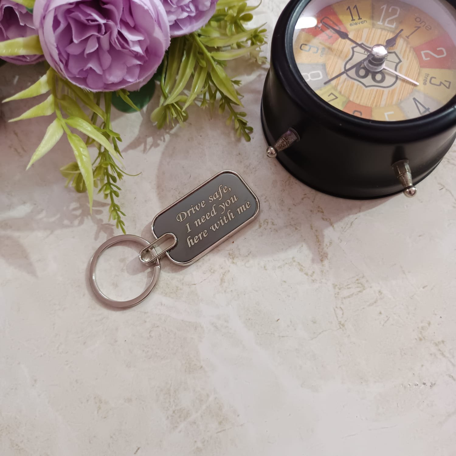 Real photo of personalised drive safe metal keychain back side engraved with custom script message "Drive safe, I need you here with me", styled with purple roses and vintage Route 66 clock