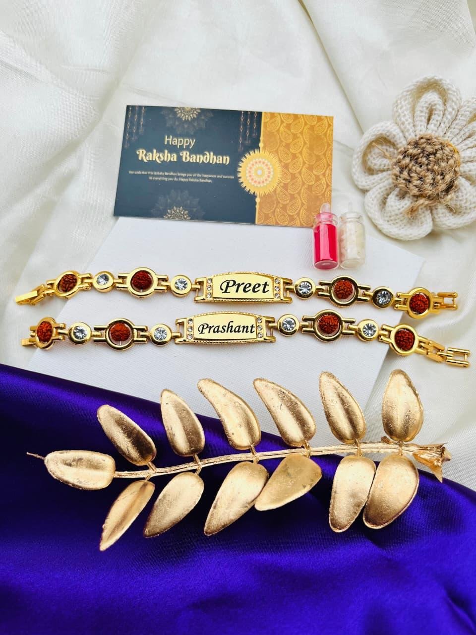 Personalised gold-tone rudraksha and crystal stone name bracelet rakhi with engraved name plate, roli-chawal vials and a Happy Raksha Bandhan greeting card
